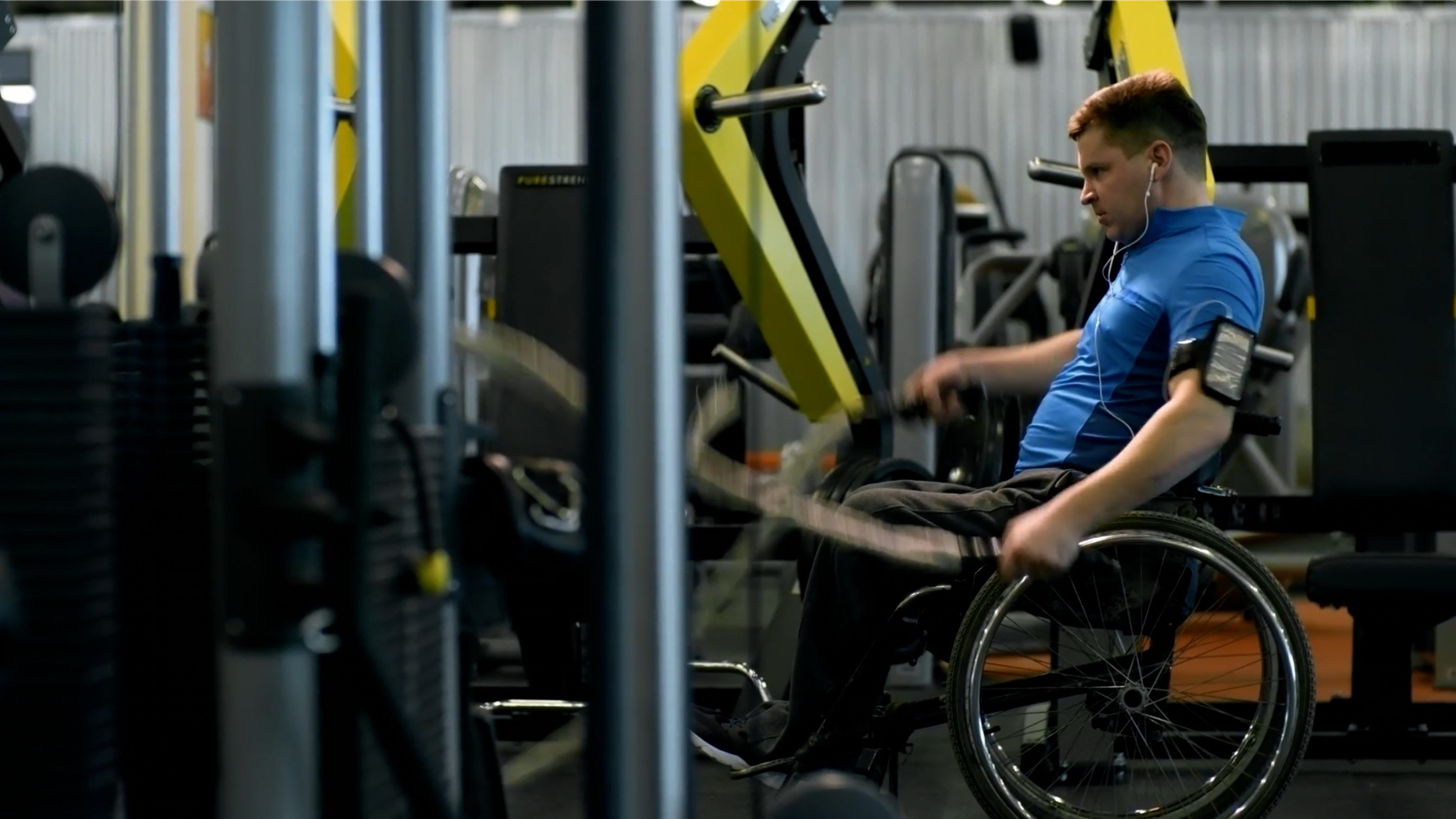 Good looking young man in a wheelchair working out with the weighted ropes, listening to music, in his wheelchair